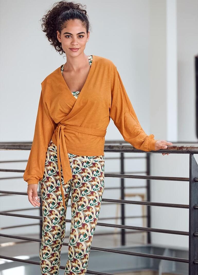 Vrouw in Mandala-outfit met wikkeljack en leggings, glimlachend.