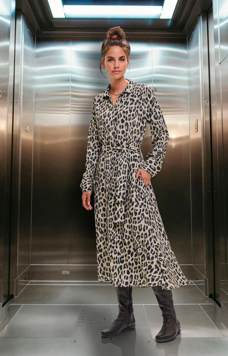 Rossana Diva jurk van wol en zijde Vrouw in een panterprint jurk staat in een lift.
