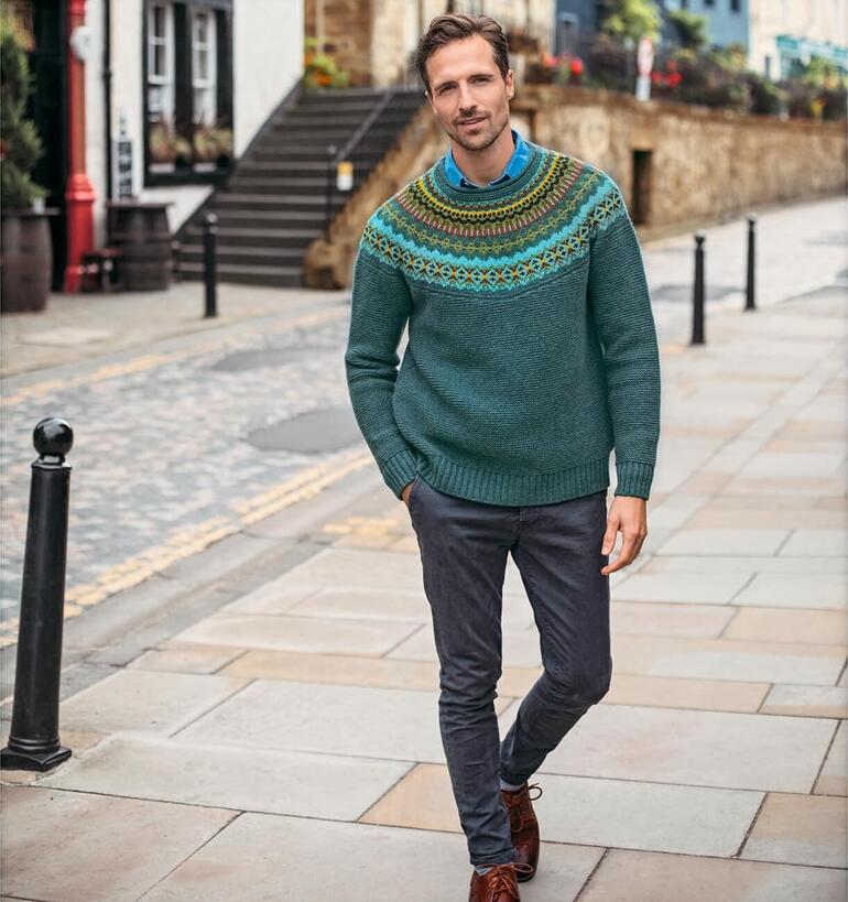 Eribé Fair Isle-trui Man in Eribé Fair-Isle trui, glimlachend voor een landelijke achtergrond.