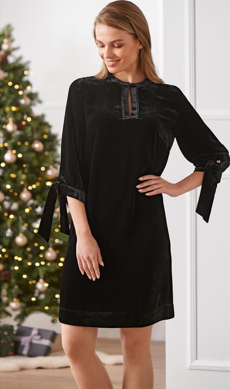 Dames tuniekjurk van zijde-velours in zwart met strikmouwen, kerstdecoratie op de achtergrond.