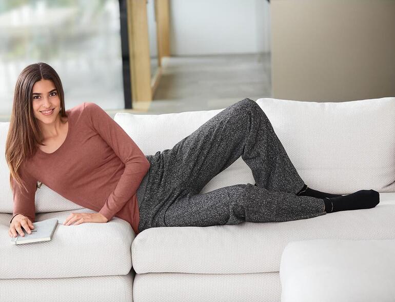 marsala Vrouw in een bruin Alpaca-Pima-shirt en grijze broek, ontspannen op de bank.