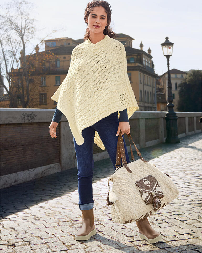bruin Vrouw in een beige gehaakte poncho met jeans buiten.