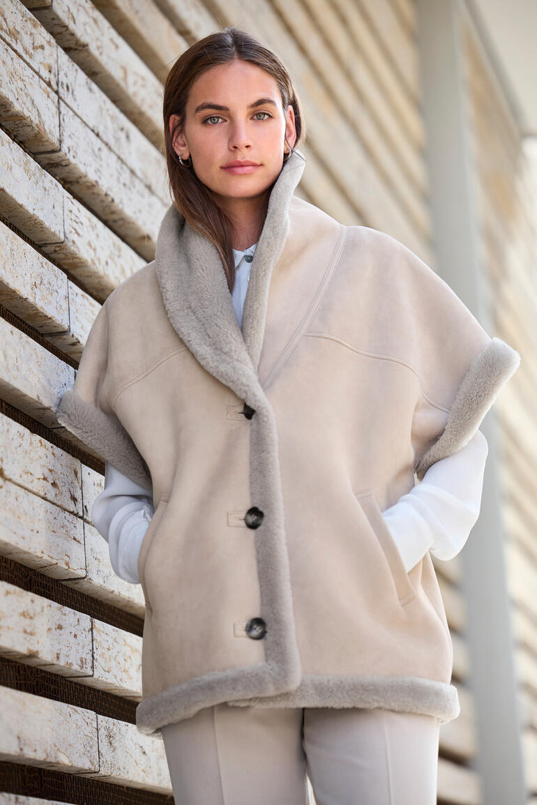 Beige lamsvelvest met opstaande kraag, gedragen door een vrouw.