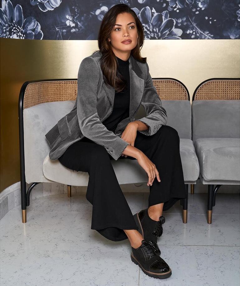 Vrouw in een fluwelen houndstooth blazer, zittend op een bank.