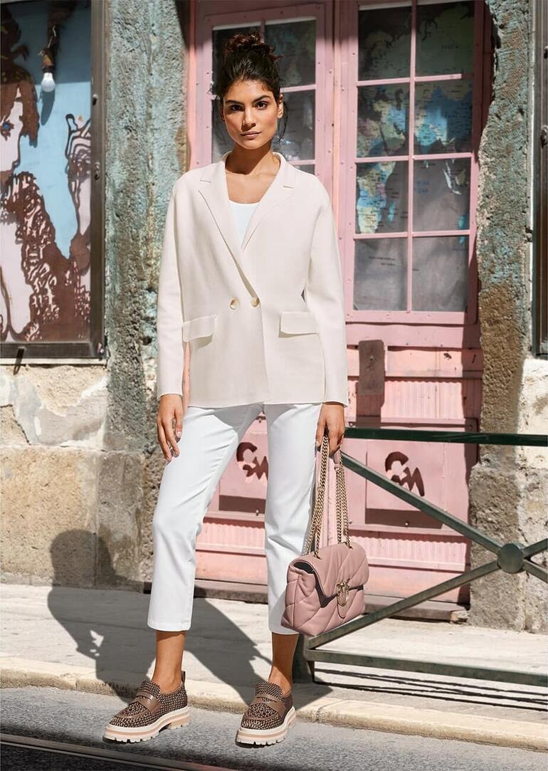 crème Vrouw in lichte blazer, bruine broek, zittend op een bank.