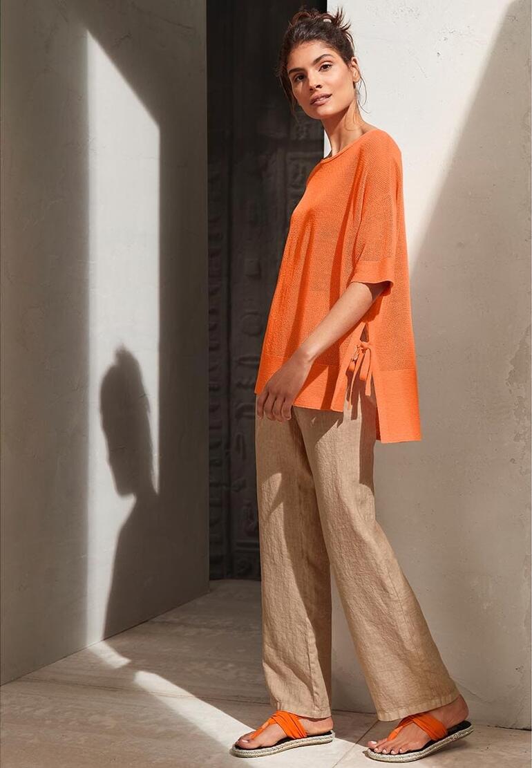 oranje Vrouw in oranje shirt en teenslippers, geposeerd in een minimalistische ruimte