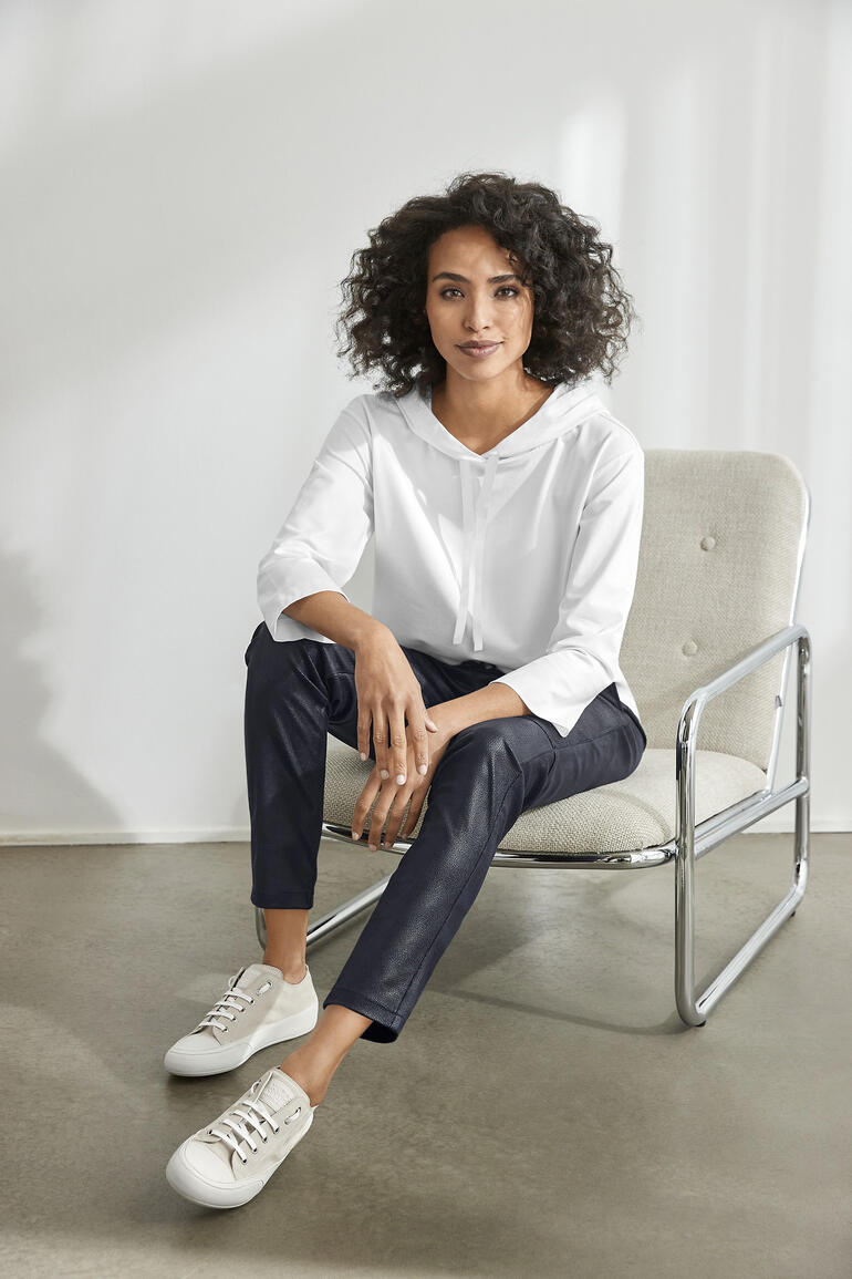 Vrouw in een witte zomer hoodie zit op een stoel