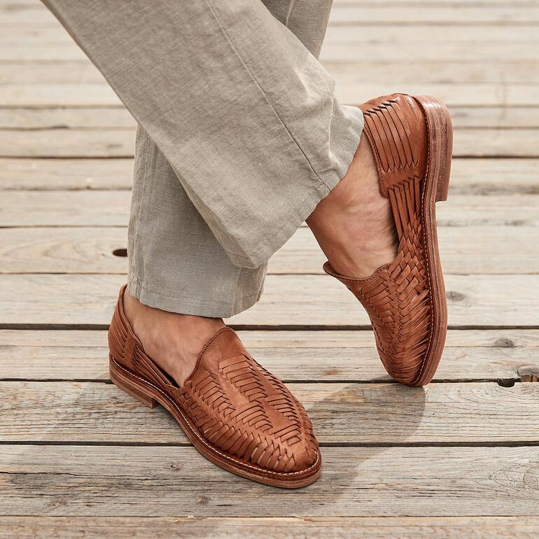 Bruine Cano gevlochten slip-on huarache, gedragen met lichte broek op houten vloer.