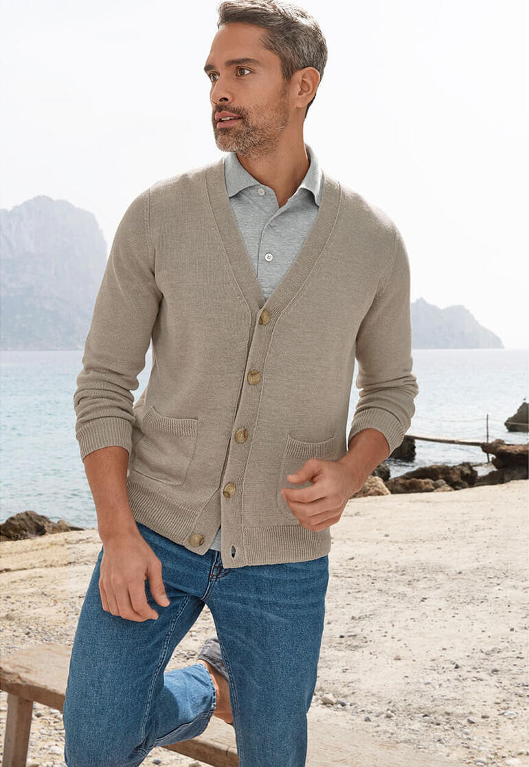 Man in linnen cardigan wandelt langs het strand