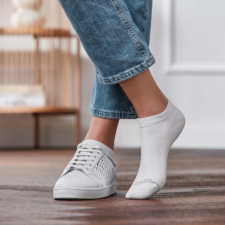 Voeten in sneakers met een witte sneakersok, zichtbaar op één voet.