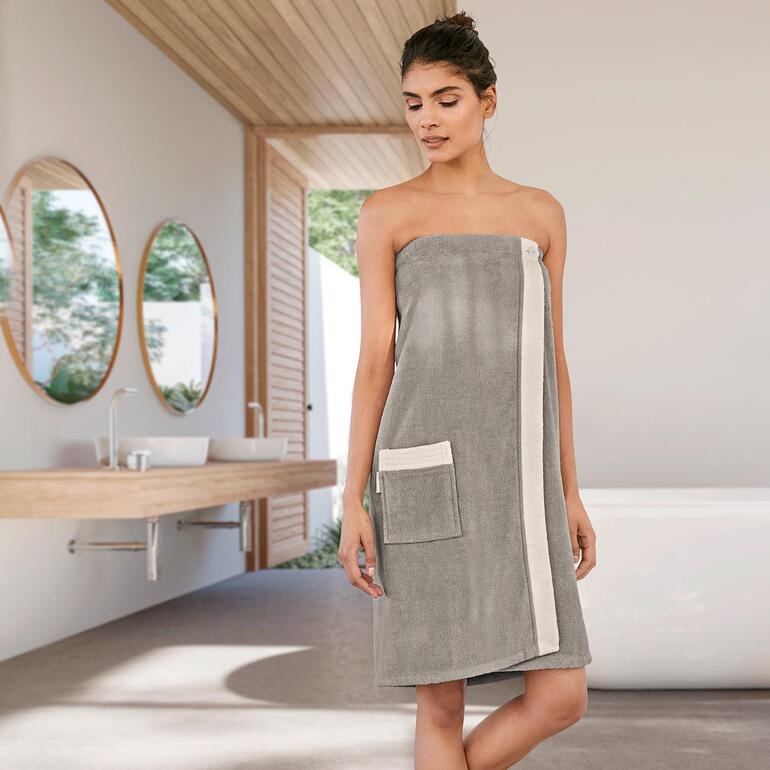 Vrouw in een grijze sauna-sarong met zijzak in een moderne badkamer.