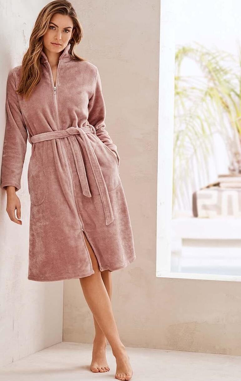 Couture-badjas Vrouw in een roze Couture badjas, staand tegen een muur.