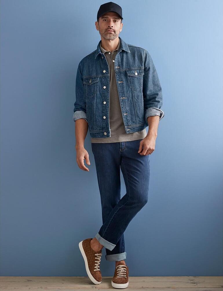 Man in hennep jeansjacke, casual voor een blauwe muur staande.