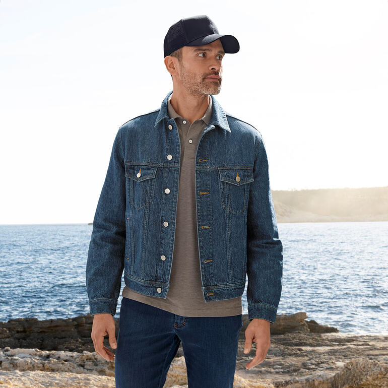 Stetson truckercap Man in OCONI hennep jeansjacke bij de zee met een grijze polo.
