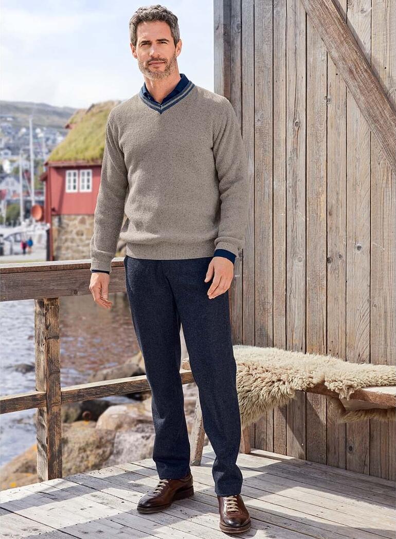 Junghans 1954 tweedtrui Man in grijze Edel-Tweed-pullover staat voor een houten gevel.