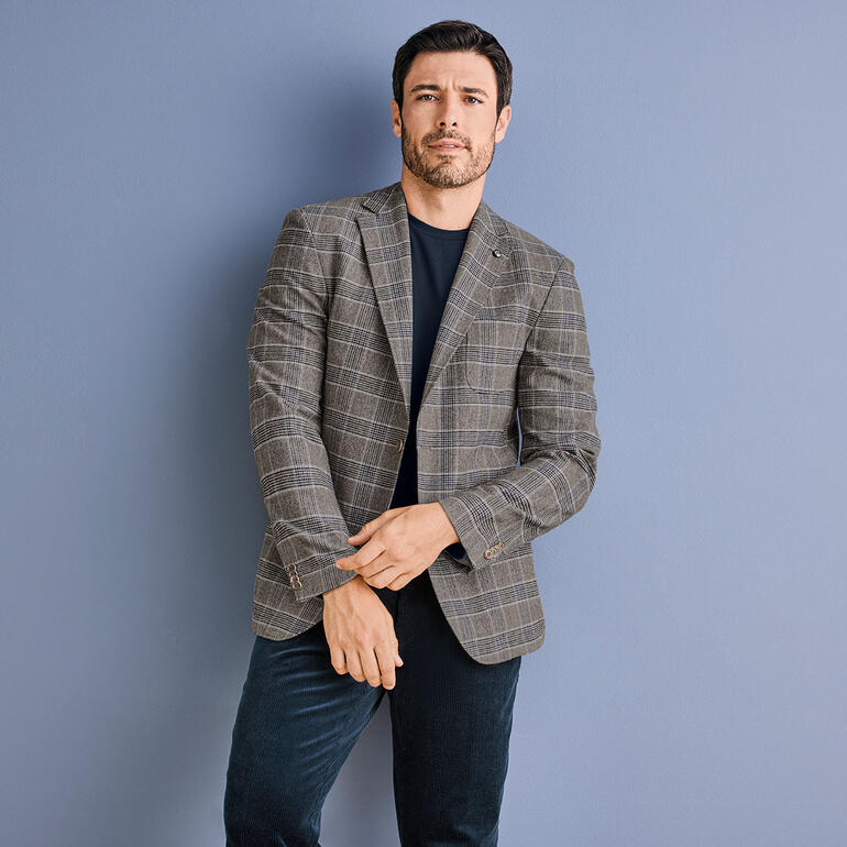 colbert Man draagt een grijs Glencheck-blazer, poseert voor een blauwe muur.