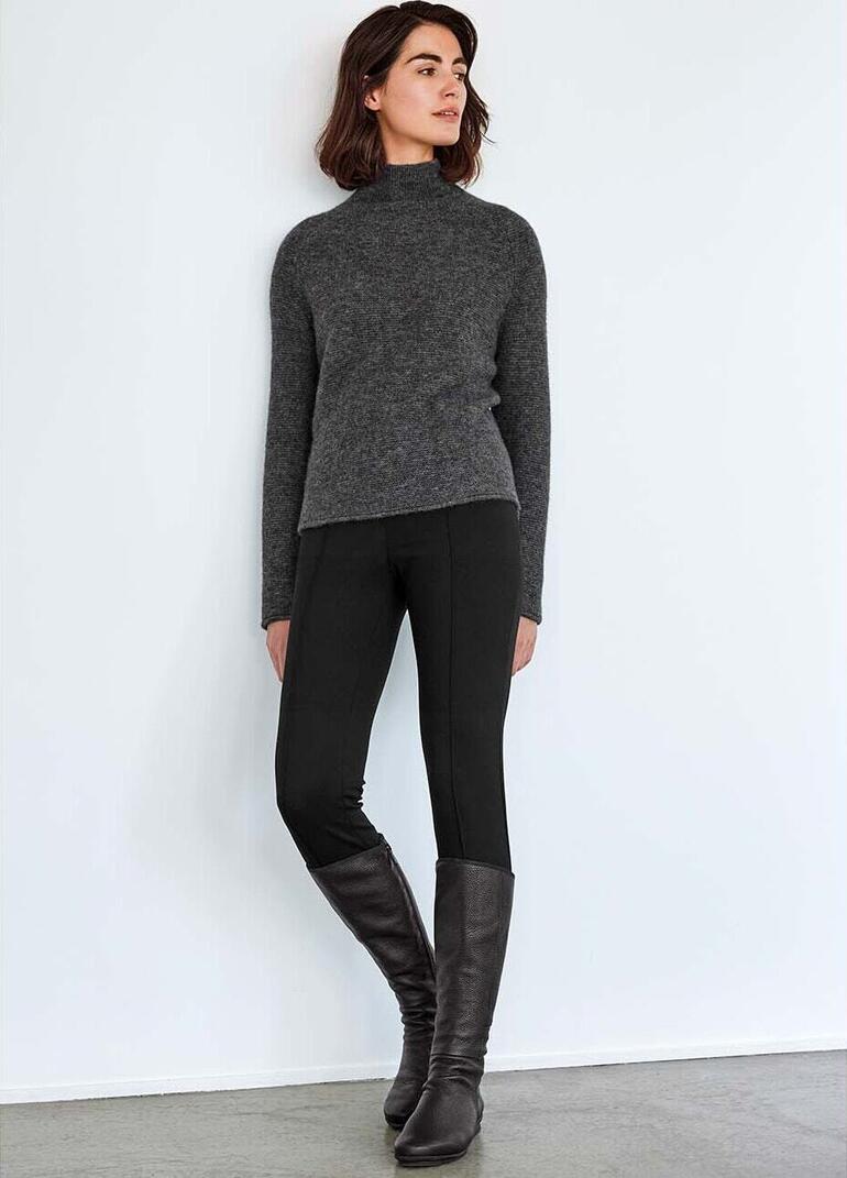 Vrouw in grijze boxy pullover en zwarte leggings.