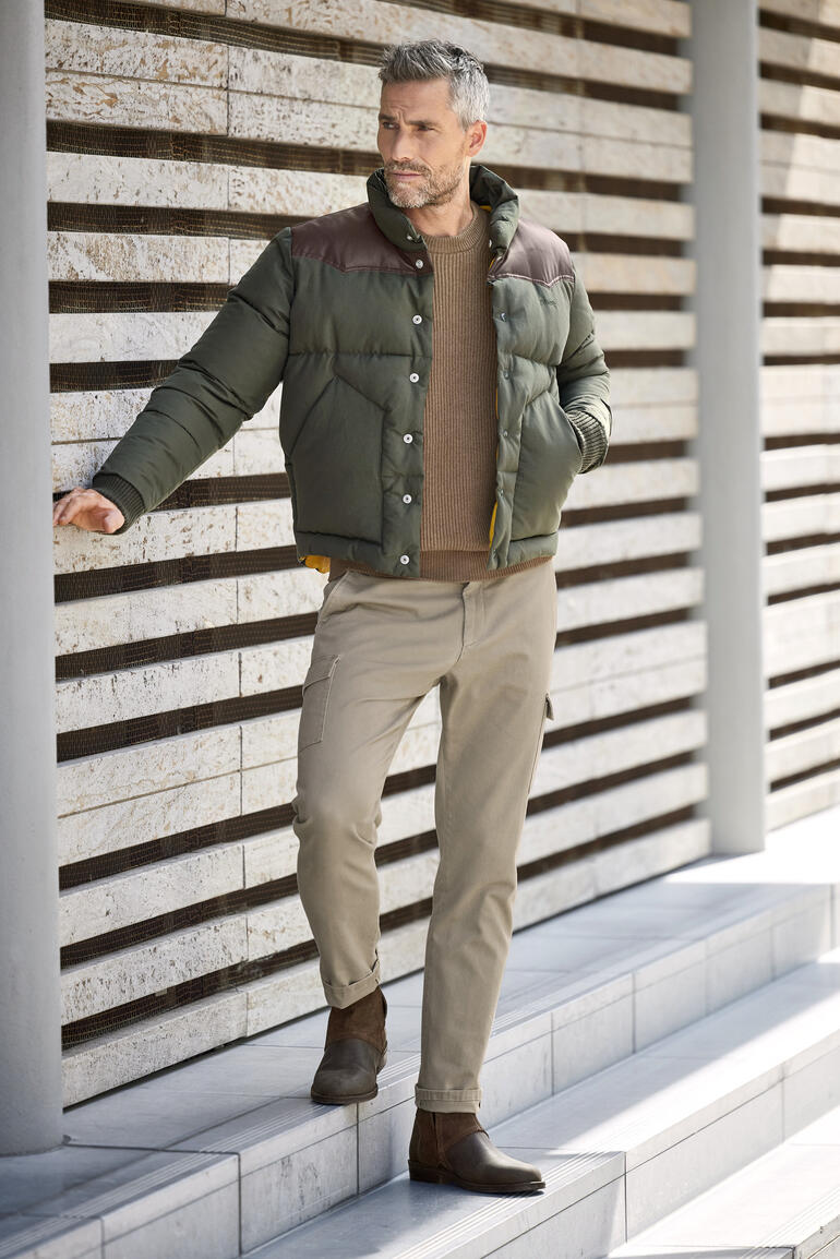 Man in kamelenhaar pullover en jas wijst naar zijn tanden.