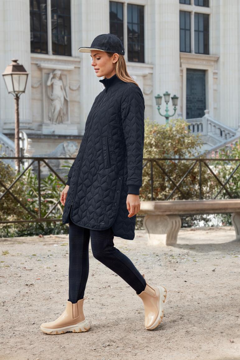 Vrouw in een zwarte gewatteerde jas loopt voorbij een historisch gebouw.