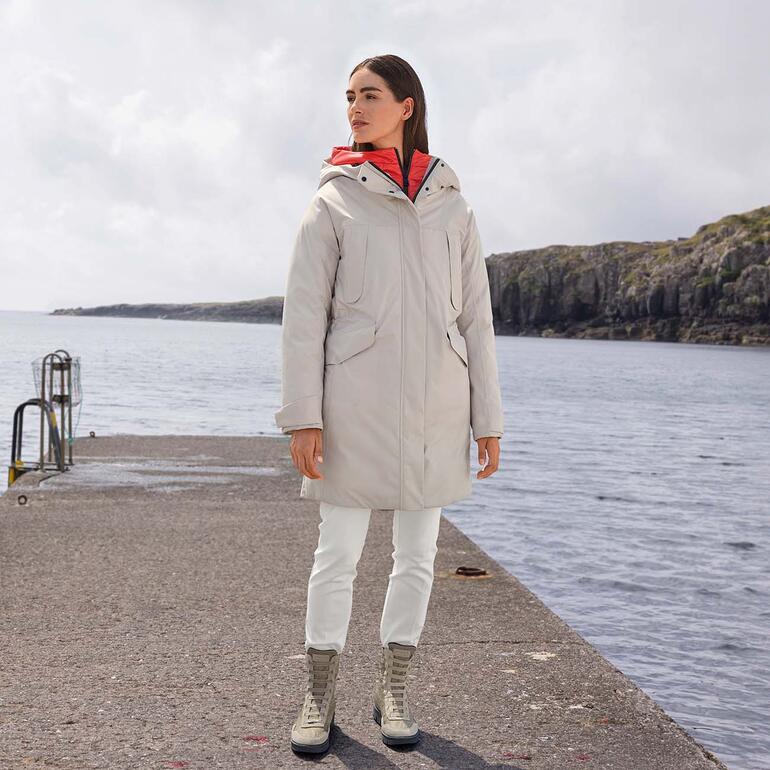 Kris Reutter ecorepel®-broek Vrouw in een grijze jas staat aan een havenpromenade.