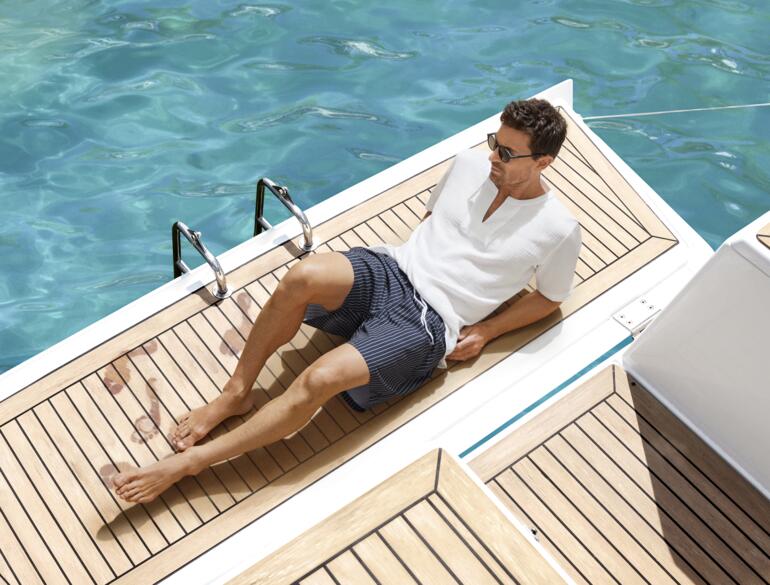 Swim&Dry-zwemshort Man in witte shorts zit op een steiger naast een zwembad.