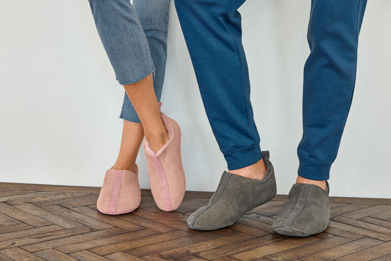 dames, roze en heren, grijs Een paar lamswollen slip-ons in roze en grijs op de vloer.