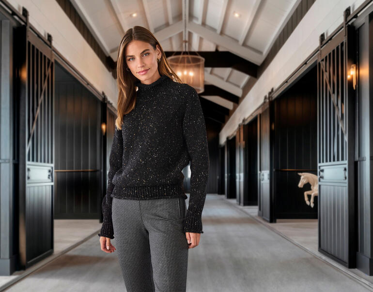 zwart Vrouw in zwarte trui en houndstooth broek in een hal met een paard op de achtergrond.