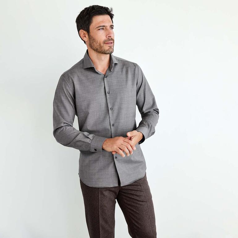 Man in een grijs Merino-performance-overhemd staat in een lichte ruimte.