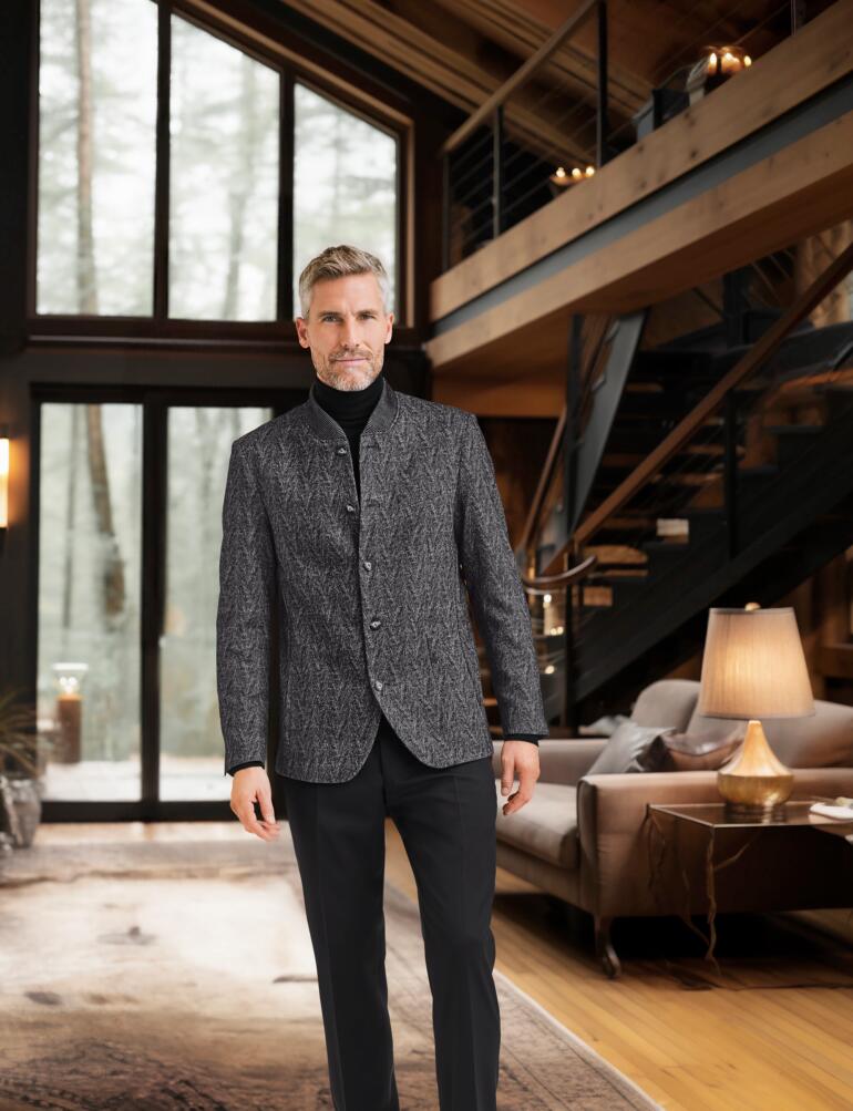 Hartwich visgraatcolbert Man in visgraat colbert, staande in een luxe kamer met details van hout.