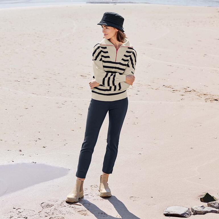 Vrouw in gestreepte merino trui en hoed op het strand.