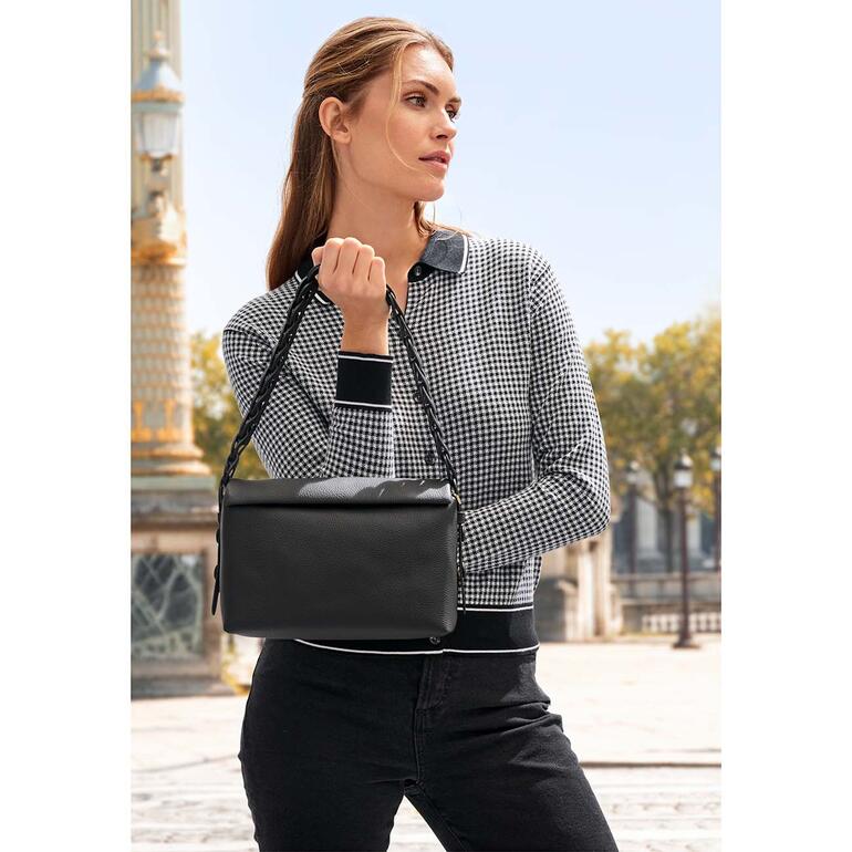 Vrouw met een zwarte handtas poseert voor een stadslandschap.