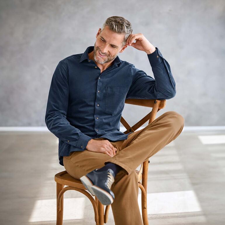Chic corduroy overhemd Man in donkerblauw corduroy overhemd zit ontspannen op een stoel.