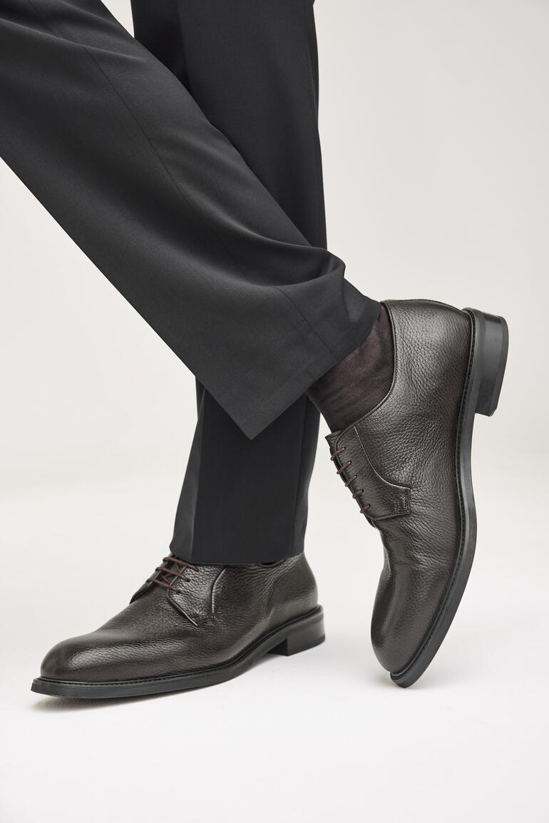 Man draagt bruine hertenleren business schoenen, half zittend in een pak.