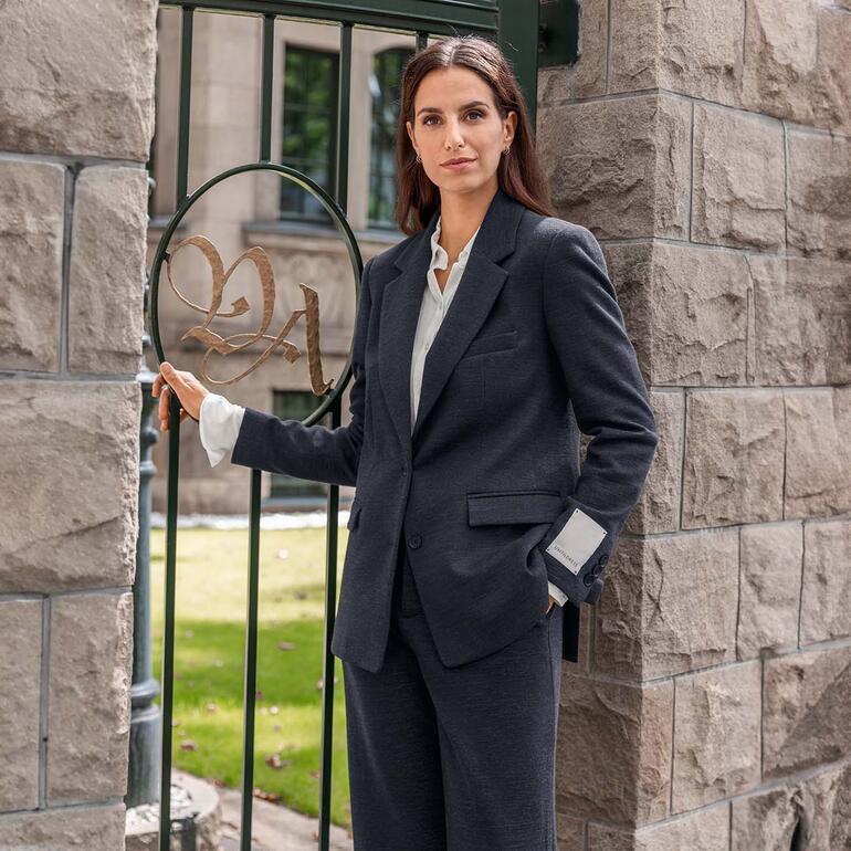 blazer en broek Portret van een vrouw in een zwarte blazer leunend tegen een pilaar.