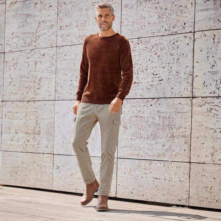 Cargobroek van dobby-stof Man draagt een bruine trui en beige Dobby-cargobroek voor een structuurwand.