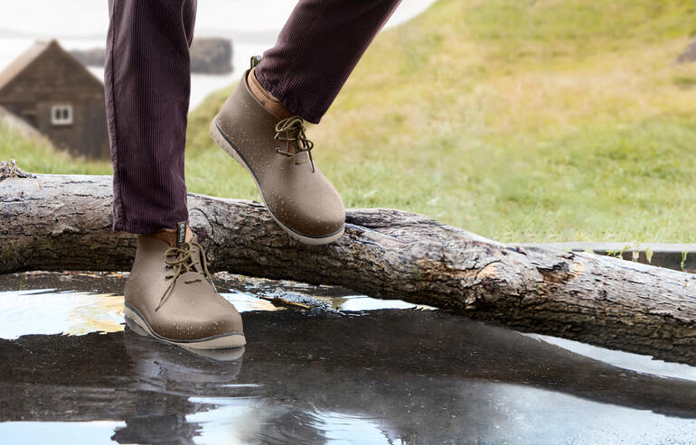 Man draagt beige Ccilu regenlaarzen en staat naast een boomstronk op water.