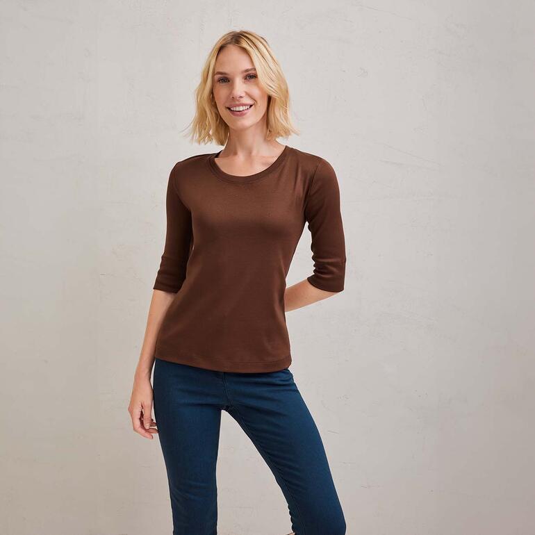 Vrouw in bruin shirt met korte mouwen poseert lachend voor een neutrale achtergrond.