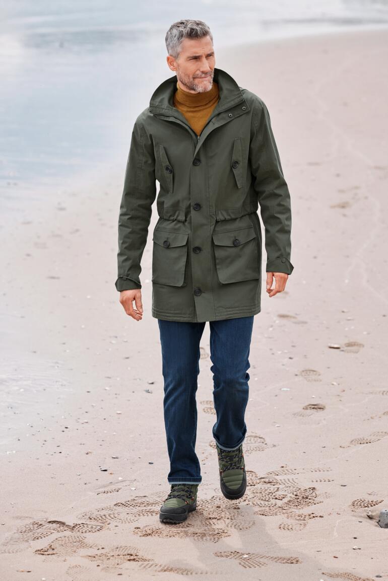 Katoenen allweather-parka Man in groene katoen parka met zakken die over het strand wandelt.