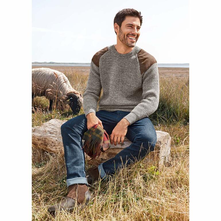 Comfortabele kasjmierjeans Man zit op een boomstam in de natuur, draagt een grijze trui.
