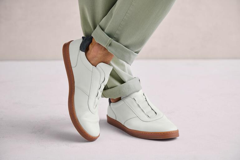 Man draagt witte OCONI slip-on schoenen op een grijze ondergrond.