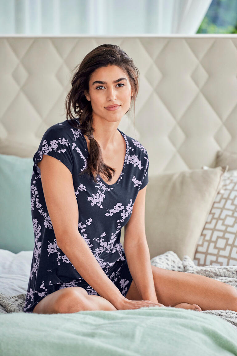 kersenbloesem Vrouw in zwart pyjama met bloemenprint zit lachend op bed.