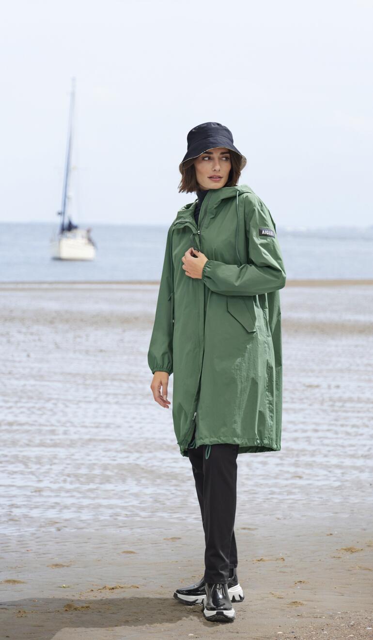 Vrouw in groene regenjas en Chelsea-sneakerboots op het strand.