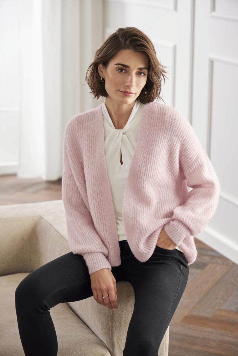 Junghans 1954 zachte cardigan Vrouw zittend in een Junghans 1954 fluffy cardigan in roze.