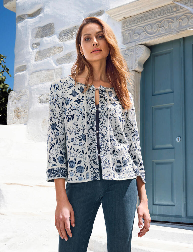 IVKO cardigan met bloemmotief Vrouw in een bloeiende cardigan voor een witte muur.