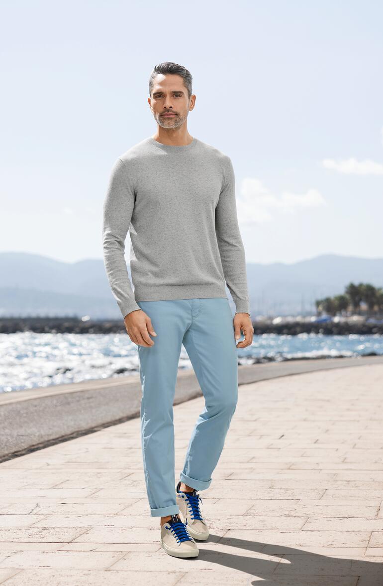 lichtblauw Man in een grijze zomer-tweed-pullover en blauwe broek op het strand.
