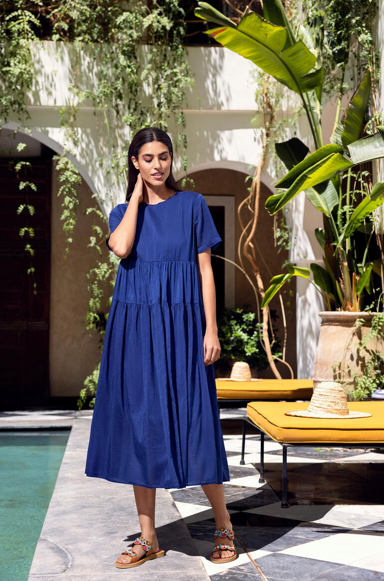 Kiltie zomerjurk van voile Vrouw in een blauwe zomerjurk staat voor een elegante achtergrond