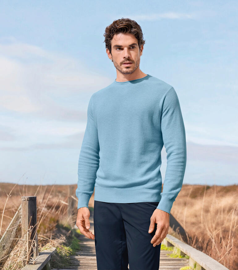 Junghans 1954 stijlvolle piqué-trui Man in een lichtblauw edel piqué sweater staat in een landelijke omgeving.