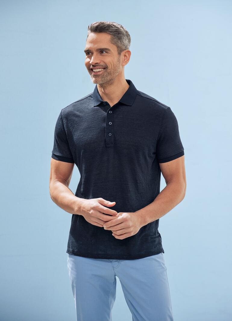 Man in zwart gekleed met een donkergrijs-blauw poloshirt op een blauwe achtergrond.