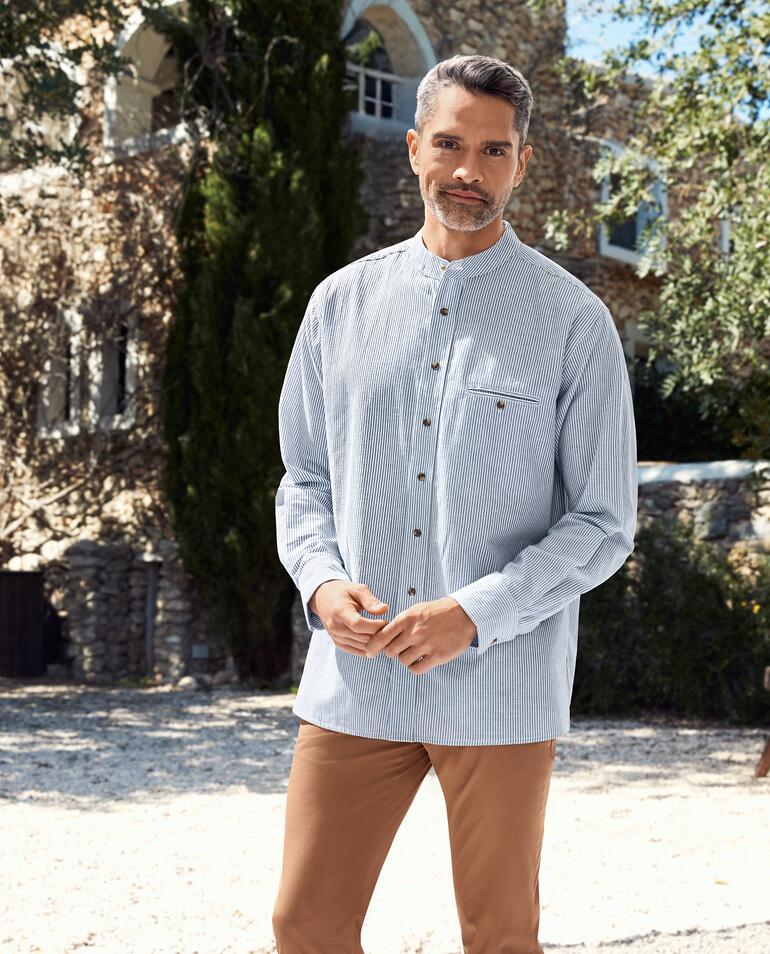 Grandfather Sunday-shirt Man met gestreepte Grandfather-shirt staat glimlachend voor een stenen achtergrond.