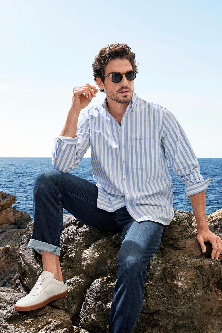 The BDO-shirt, Limited Edition No. 73 Man in gestreepte blouse zit op een steen aan zee, draagt een zonnebril.